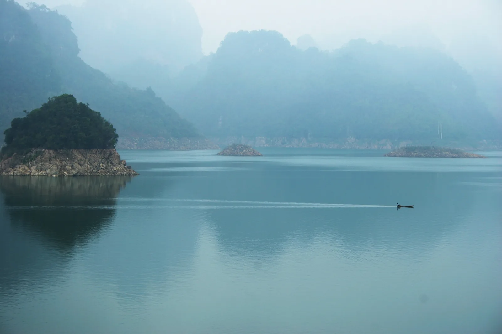 Một chiếc thuyền nhỏ lướt qua mặt nước mờ sương của hồ Sông Đà, giữa những đảo đá vôi phủ cây xanh ở Thung Nai. Một chiếc thuyền nhỏ lướt qua mặt nước mờ sương của hồ Sông Đà, giữa những đảo đá vôi phủ cây xanh ở Thung Nai.