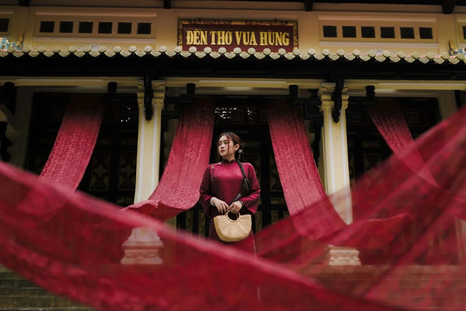 Người phụ nữ mặc áo dài đỏ đứng trước Đền Thờ Vua Hùng với dải lụa đỏ bay ở Phú Thọ. Người phụ nữ mặc áo dài đỏ đứng trước Đền Thờ Vua Hùng với dải lụa đỏ bay ở Phú Thọ.