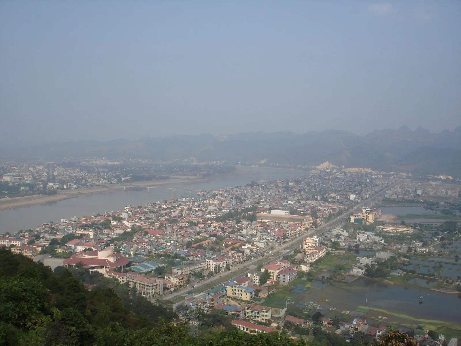 Toàn cảnh một thị trấn ven sông ở Hòa Bình nhìn từ trên cao với núi mờ sương và ruộng lúa.