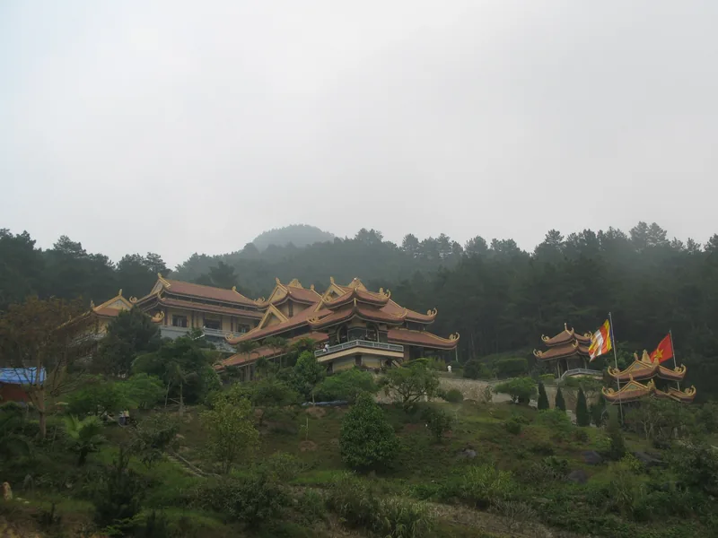Một khu chùa với mái ngói cong nằm trên đồi rừng thông gần Tam Đảo trong tiết trời sương mù.